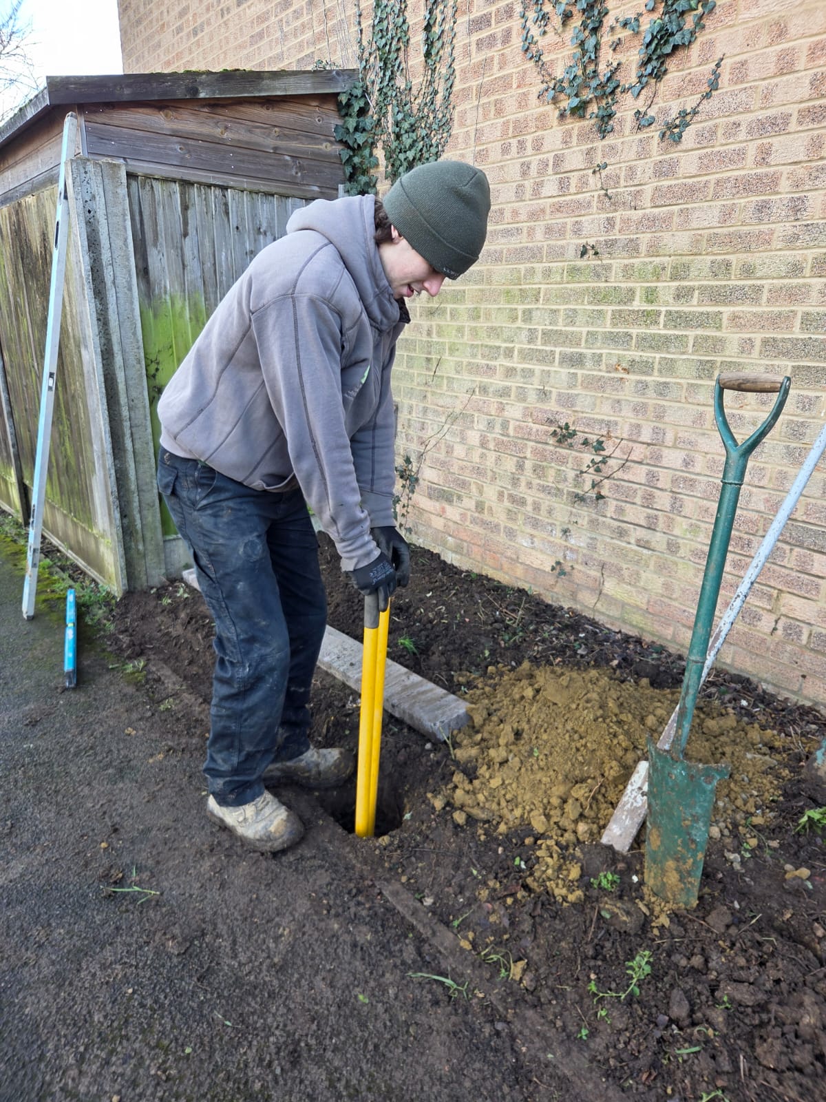 Landscaper preparing a fence post hole beside a brick house